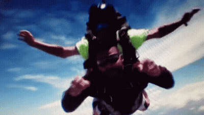 Man In Green Shirt Flying Through Blue Sky GIF