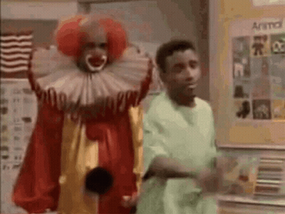 Man In Green Shirt Next To Clown In Red And Yellow Costume GIF