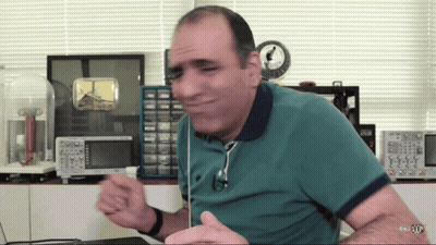 Man In Green Shirt Sitting At Desk With Clock GIF