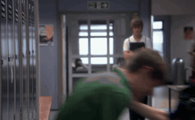 Man In Green Shirt Standing In Front Of Lockers With Fire Exit Sign GIF
