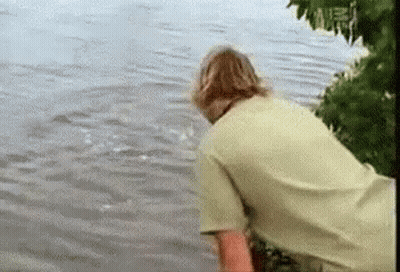 Man In Green Shirt Standing In Water Looking At Shark GIF
