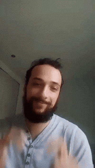 Man In Green Sweater With Sun Sits In Crowd GIF
