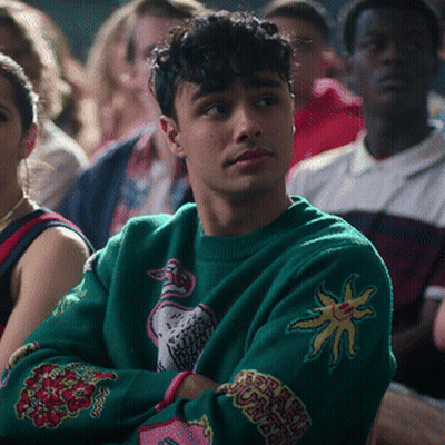 Man In Green Sweater With Sun Sits In Crowd GIF