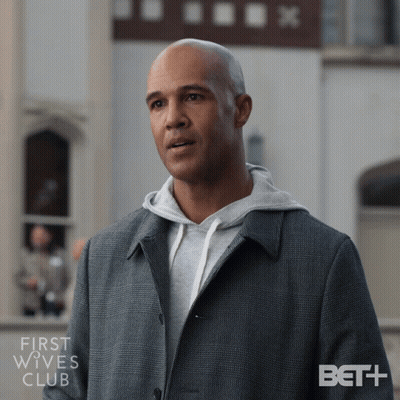 Man In Grey Coat And Hoodie In Front Of First Wives Club Building GIF