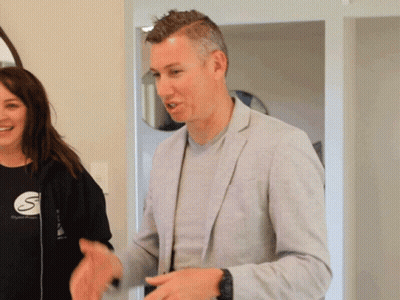 Man In Grey Jacket Next To Woman In Black Shirt With Letter S GIF