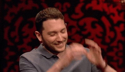 Man in Grey Shirt Clapping in Front of Red Wall