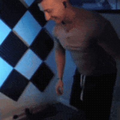 Man In Grey Shirt In Front Of Checkered Wall GIF