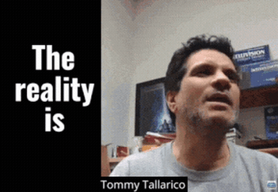 Man In Grey Shirt In Front Of Sign Saying The Reality Is Tommy Tallarico GIF