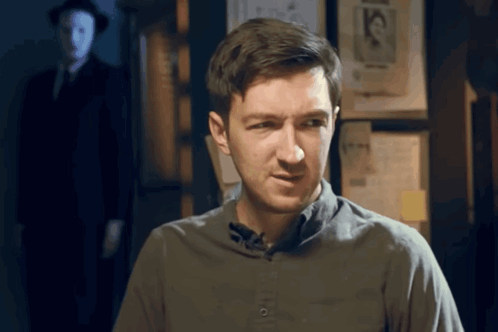 Man In Grey Shirt In Front Of Wall With Mask Picture GIF