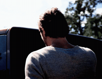 Man In Grey Sweater In Front Of Black Vehicle GIF