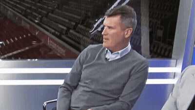 Man In Grey Sweater Sitting In Front Of Stadium Sign GIF