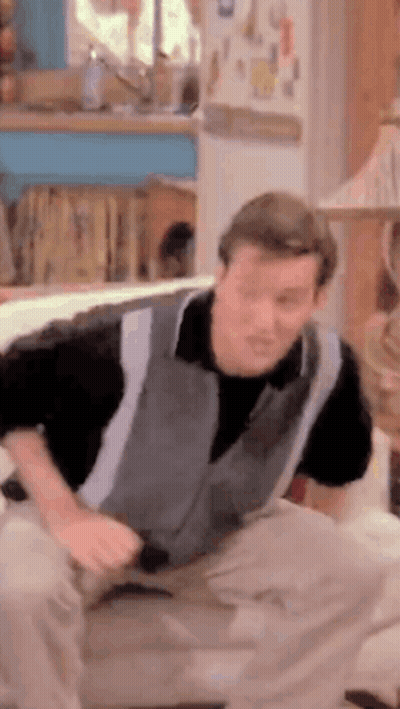 Man In Grey Vest Sitting On Couch GIF