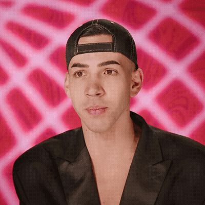 Man In Hat And Black Jacket Looks At Camera GIF