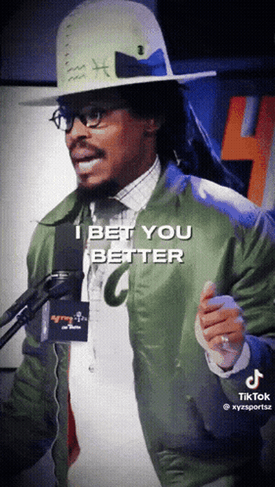 Man In Hat And Green Jacket Talking Into Microphone GIF