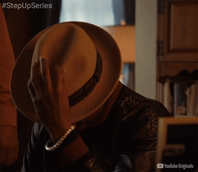 Man In Hat And Leather Jacket Sitting In Front Of YouTube Originals Sign GIF