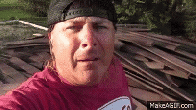 Man In Hat And Red Shirt Next To Wood Pile GIF