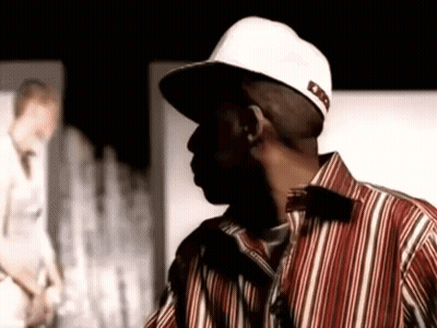 Man In Hat And Striped Shirt Standing Before Wall GIF