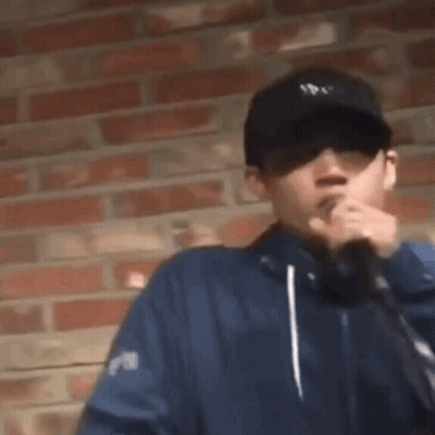 Man In Hat And Sunglasses Smoking By Brick Wall GIF