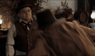 Man In Hat And Vest Talking To Man In Brown Coat GIF