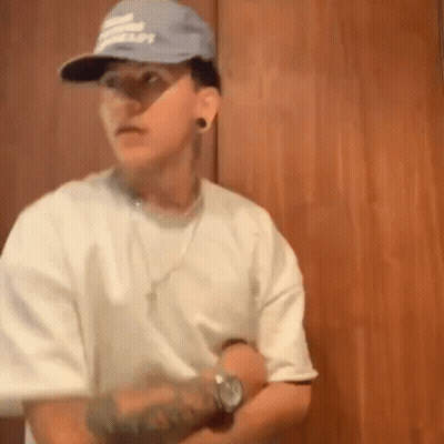 Man In Hat And White Shirt Standing In Front Of Wooden Door GIF
