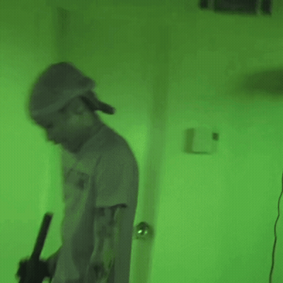 Man In Hat Holding Gun In Green Lit Room GIF