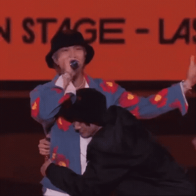 Man In Hat Hugging Man In Front Of Stage Sign GIF