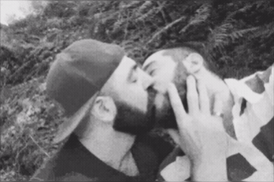 Man In Hat Kissing Another Man On Cheek GIF