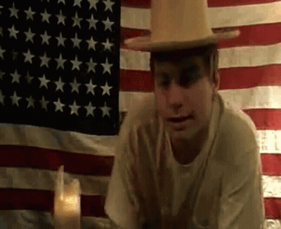 Man In Hat Sitting In Front Of American Flag GIF