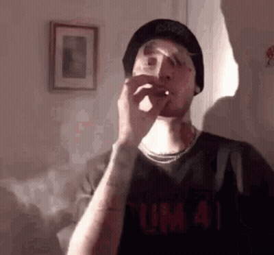 Man In Hat Smoking Cigarette In Living Room GIF