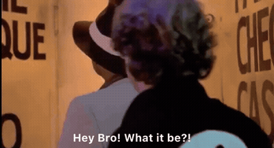 Man In Hat Talking To Man At Sign Hey Bro What It Be GIF