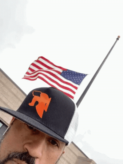 Man In Hat With Letter R In Front Of Flag GIF