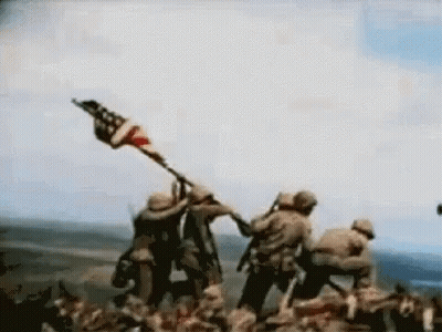 Man In Hat With Letter R Standing Before Flag GIF