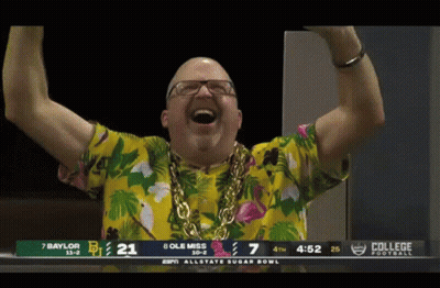 Man In Hawaiian Shirt And Gold Chain In Front Of College Football Scoreboard GIF