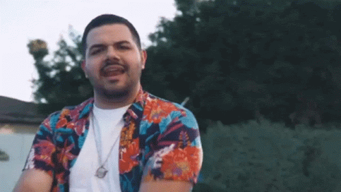 Man In Hawaiian Shirt And Necklace Standing In Front Of Trees GIF