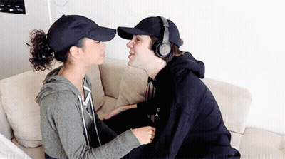 Man In Headphones And Baseball Cap Kissing Woman On Cheek GIF