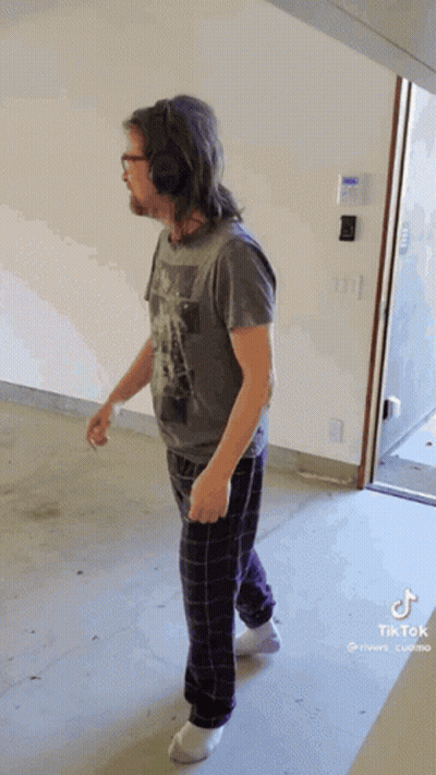 Man In Headphones And Pajama Pants Walking In Hallway GIF