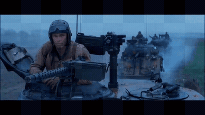 Man In Helmet Holding Machine Gun In Front Of Tanks GIF