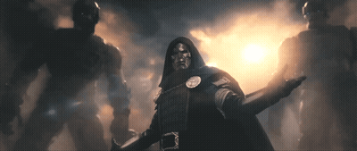 Man In Hooded Cape In Front Of Giant Robots GIF