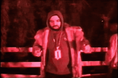 Man In Hooded Jacket By Fence In Dark Room GIF