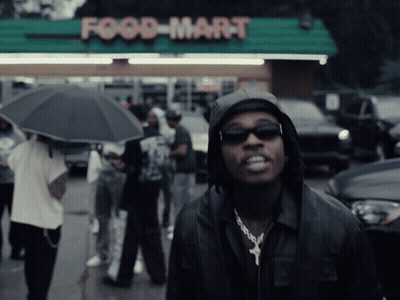 Man In Hooded Jacket In Front Of Food Mart GIF
