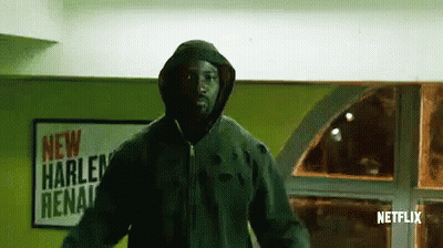 Man In Hooded Jacket In Front Of New Harlem Arena Sign GIF