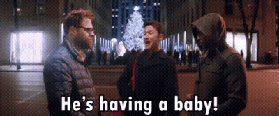Man In Hooded Jacket Says Having A Baby In Front Of Christmas Tree GIF