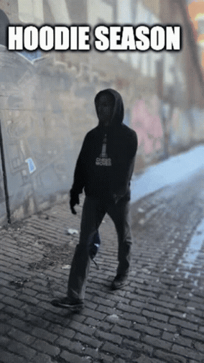 Man In Hoodie Walking Down Cobblestone Street GIF