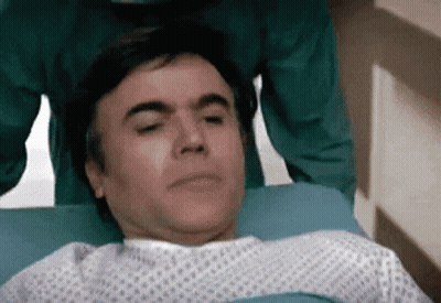 Man In Hospital Gown Laying With Eyes Closed GIF