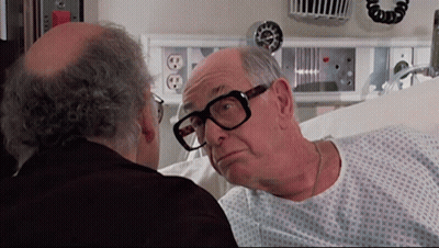 Man In Hospital Gown Looking At Man With Glasses GIF