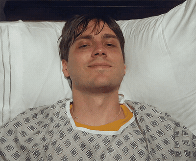 Man In Hospital Gown Smiling In Bed GIF