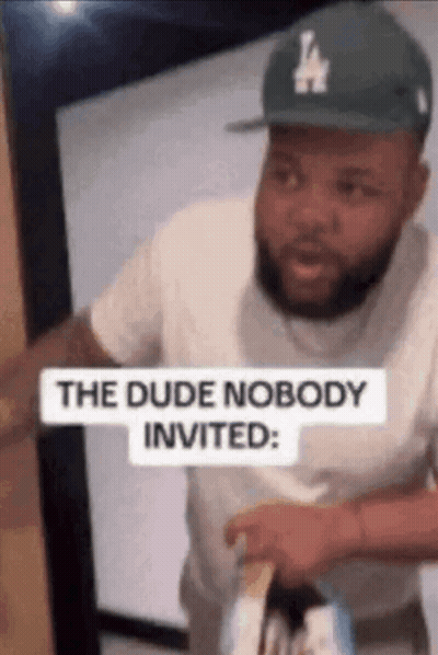Man In LA Hat Standing In Doorway With Sign The Dude Nobody Invited GIF