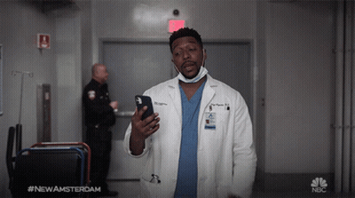 Man In Lab Coat Holding Cell Phone In Front Of NBC Sign GIF