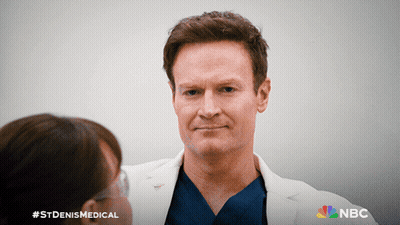 Man In Lab Coat Talking To Woman With NBC Logo GIF