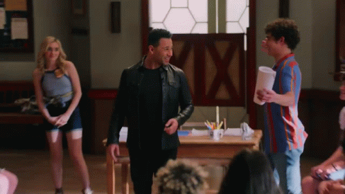 Man In Leather Jacket Standing In Front Of Group Talking To Another Man GIF